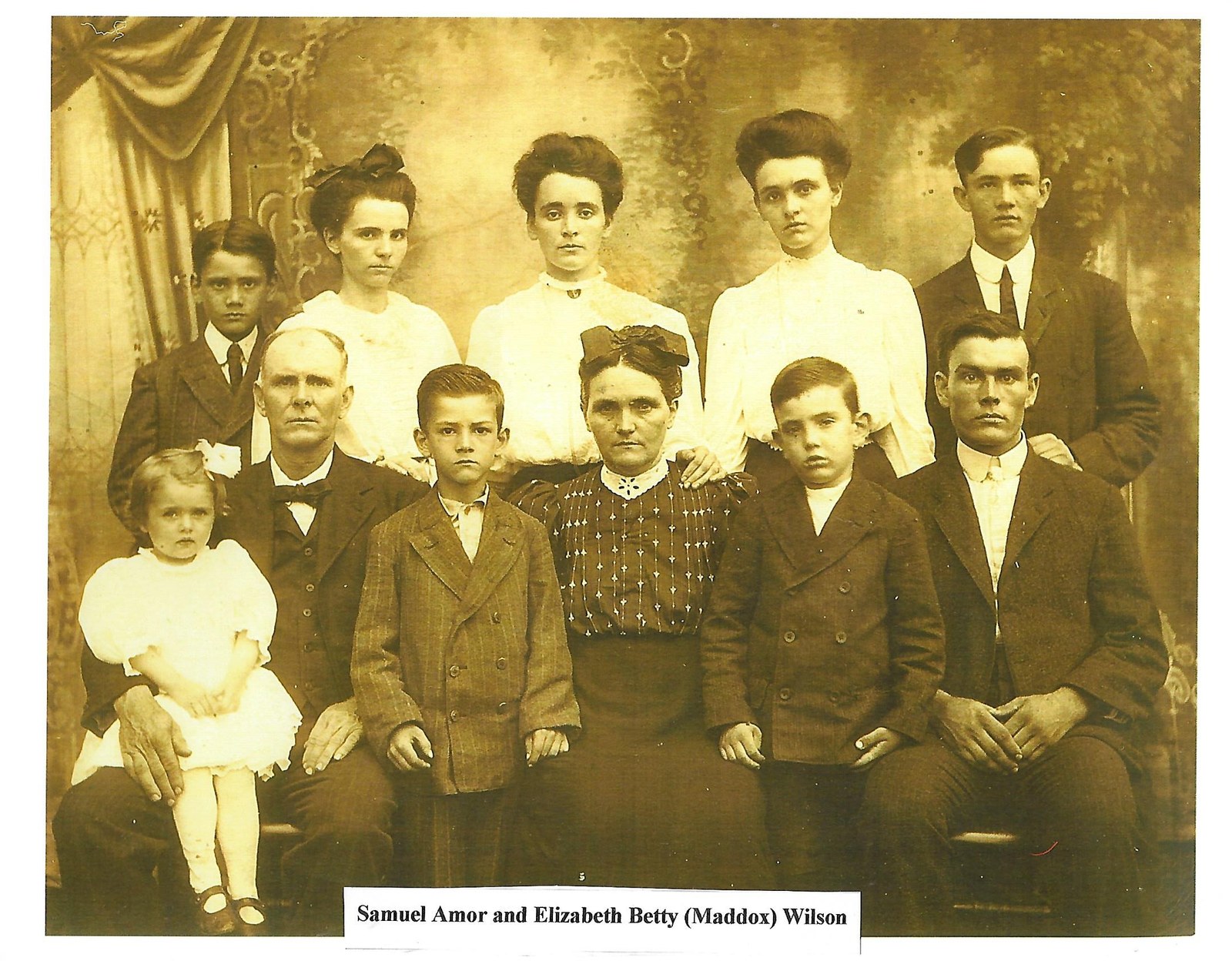 Archival scan crop showing samuel Amor and Elizabeth Betty Maddox Wilson family. Front row, left to right: Velma, Samuel, Glen, Elizabeth, Ralph, and Charles Wilson. Back row: Walter, Olive, Lorella, Ethel, and Homer Wilson.